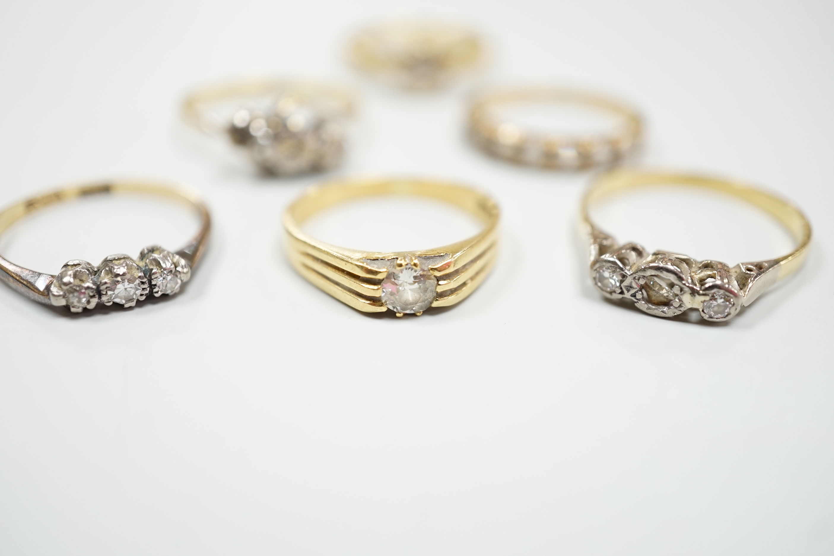 Six assorted gold dress rings, comprising an 18ct gold and platinum three stone ring, size O, an 18ct gold claw set solitaire diamond ring, size O, an 18ct gold illusion set solitaire diamond ring, size L, an 18ct gold t